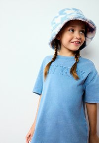 T-shirt en coton bleu clair avec des manches courtes et un brodé en relief "NY". Associée à un chapeau seau en peluche bleu et blanc à motifs.
