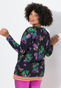 Maglione nero con vivaci draghi verdi e fiori viola. Ha un orlo a righe multicolori e una vestibilità rilassata.