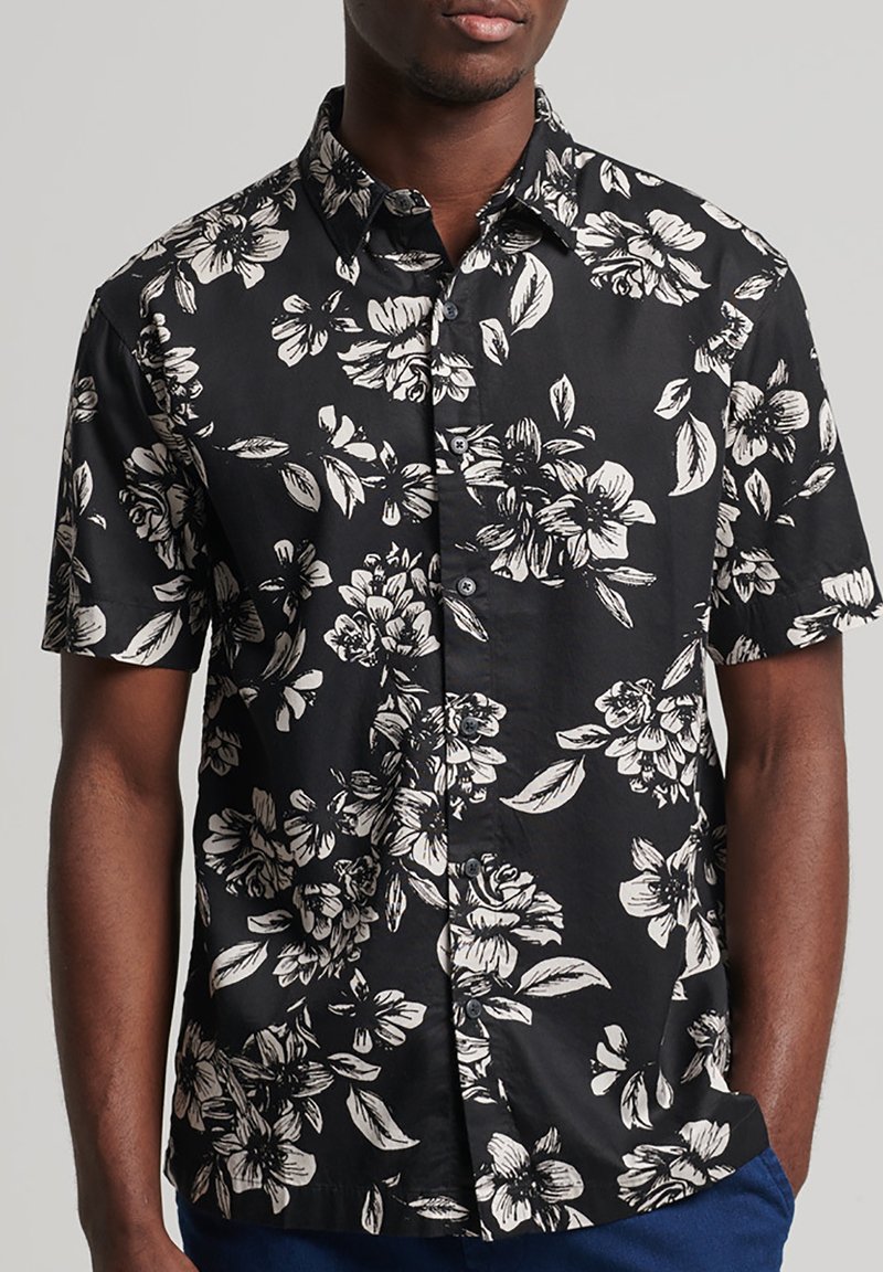 Chemise noire à manches courtes avec imprimé floral blanc, col à boutons, tissu léger et coupe décontractée. Design minimaliste avec boutons classiques.