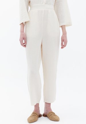 Pantalon blanc texturé avec une coupe ample, taille plate et chevilles fuselées. Associé à des chaussures à enfiler tissées de couleur beige.