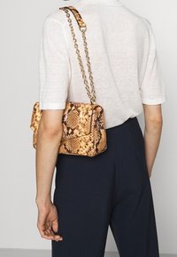 Torebka w wzór węża w odcieniach złota i brązu z łańcuszkowym paskiem. Kompaktowy design z klapą i teksturowaną powierzchnią.