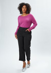 Fuchsia Pullover mit gerippter Textur und Bündchendetails, kombiniert mit schwarzen, taillierten Hosen mit eingelegten Bügelfalten und silbernen Plateausandalen.
