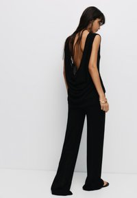 Top nero senza maniche con design a schiena drappeggiata, abbinato a pantaloni neri larghi e morbidi. Tessuto liscio, accenti minimi e vestibilità comoda.