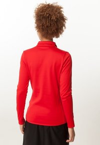 Top rojo de manga larga con un diseño ajustado y un cuello tipo mock, fabricado en tejido suave. Espalda sin costuras, sin accesorios o patrones visibles.