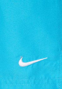 Élénk kék Nike anyag, fehér hímzett swoosh logóval. Simább textúra, varrott részletekkel a varrat mentén.