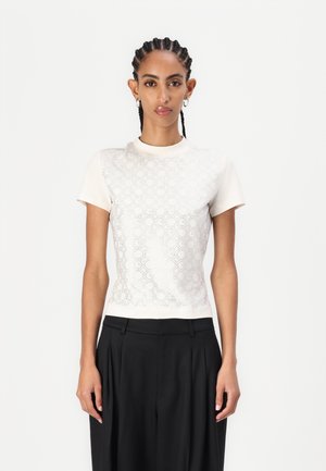 Short-sleeve, fitted top in light beige with a textured, patterned front. Rounded neckline and smooth fabric. Paired with high-waisted black trousers.
