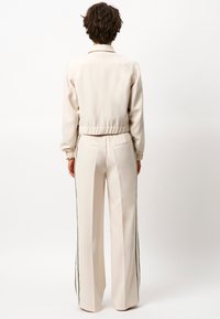 Beige trainingsjack en wijde broek met zwarte zijstrepen, met een cropped zoom, elastische manchetten en achterzakken.