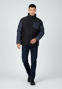 Kurtka pikowana z czarnym, pikowanym korpusem i dżinsowymi rękawami, wyposażona w kieszeń na piersi, zapięcie na zamek oraz dwie przednie kieszenie. Granatowe spodnie i buty.
