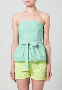 Top senza spalline verde menta con texture ad occhiello, design a peplum, cuciture verticali e un fiocco in vita; abbinato a pantaloni corti giallo chiaro.