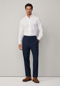 Camicia bianca con bottoni, pantaloni eleganti blu scuro e scarpe in pelle marrone. La camicia ha un colletto e maniche lunghe; vestibilità liscia e su misura.