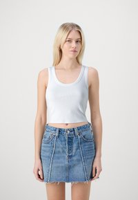 Hvid ribbet crop top med rund halsudskæring parret med en blå denim mini nederdel med frynset kant og bleget pletter.
