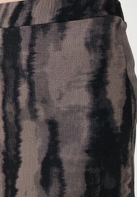Falda de tejido acanalado en tonos marrones y negros con un patrón de tie-dye. Presenta una textura suave y una forma estilizada.