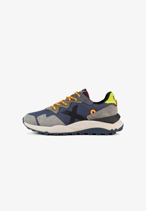 Zapatillas deportivas en gris, azul marino y naranja. Materiales mixtos con malla y gamuza, con una gruesa suela blanca y una base de tracción de goma.