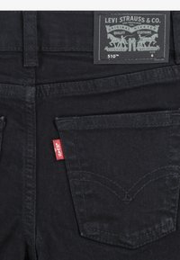 Black denim jeans with a five-pocket design. Features a red logo tag on the back pocket and a dark fabric label with brand details.
