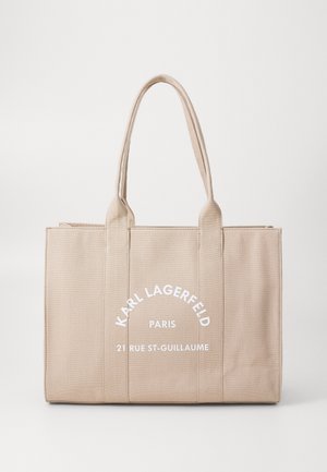 Sac cabas beige avec deux poignées avec texte blanc : Karl Lagerfeld Paris 21 Rue St-Guillaume au centre devant.