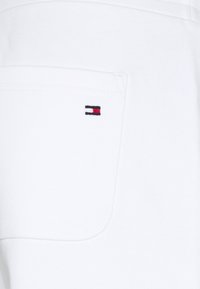 Vitt bomullstyg med en lapplomme. Har en liten broderad logotyp i blått, rött och vitt på fickans kant.