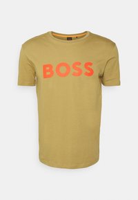 Olivově zelené tričko vyrobené z bavlny, s kulatým výstřihem a krátkými rukávy. Na hrudi se nachází výrazný oranžový nápis "BOSS". Hladká textura.