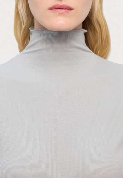 Heleda hallhallilõikega heledashall turtleneck, mis on tihedalt istuv ja pehme tekstuuriga. Krae on servadest veidi kogutud.