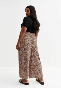 Zwarte top met korte mouwen gecombineerd met beige en bruine broek met wijde been, met een elastische tailleband en een textuurstof.