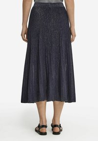 Marinblå plisserad kjol med metallisk glans. Har resårmidja och når till mitt på vadbenet. Bärs med svarta sandaler.