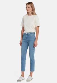 T-shirt in cotone crema con maniche corte, abbinato a jeans a vita alta di colore blu chiaro e sneakers bianche. Design semplice, senza motivi visibili.