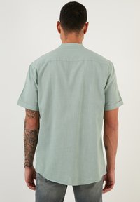 Camisa de manga corta de color verde claro hecha de una tela texturizada, con un dobladillo recto y un diseño de yugo en la parte posterior.