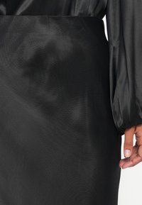 Tafetă neagră cu o textură netedă, având un design cu talie înaltă și mâneci ample. Îmbrăcămintea are un luciu subtil și o cădere elegantă.