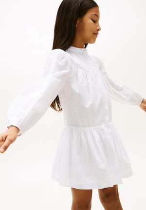 Robe en coton blanc avec broderie florale, col rond, fermeture à boutons, manches longues bouffantes et jupe évasée. Texture de tissu lisse.