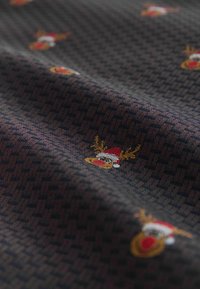 Tessuto scuro con un motivo geometrico testurizzato, decorato con renne ricamate multicolori che indossano cappelli di Babbo Natale.