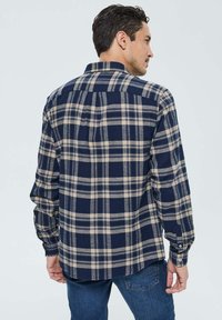 Chemise en flanelle à carreaux bleu marine et beige avec col boutonné et manches longues. Comprend un empiècement et des poignets cousus.