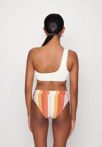 Top de biquíni branco canelado de um ombro só, combinado com parte de baixo de biquíni de cintura alta listrada em várias cores em tons quentes.