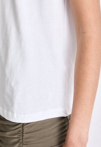 T-shirt bianco in cotone con scollatura rotonda e maniche corte; presenta un piccolo logo ricamato vicino all'orlo. Tessuto liscio, vestibilità casual.