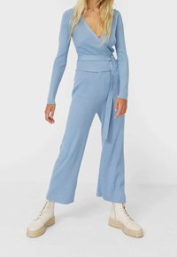 Hellblaues, geripptes Strick-Zweiteiler mit einem Wickeloberteil und weit geschnittenen Hosen, kombiniert mit beigen Schnürstiefeln.