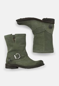 Botines de ante verde hasta el tobillo con una correa decorativa y hebilla, puntera redondeada, caña de altura media y tacón de bloque de madera. Textura suave.