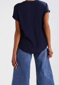 Top blu navy a maniche corte con scollo rotondo, taglio rilassato e tessuto morbido. Indossato con jeans di denim blu chiaro a gamba larga.