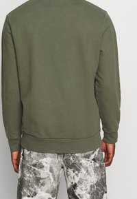Sweatshirt vert olive avec un col rond, des poignets et un ourlet côtelés. Associé à un jean gris marbré avec une texture usée.
