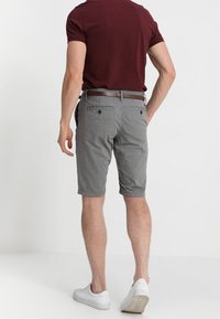 Shorts gris en tissu texturé, dotés de deux poches arrière à bouton. Associés à une chemise à manches courtes bordeaux et des baskets blanches.