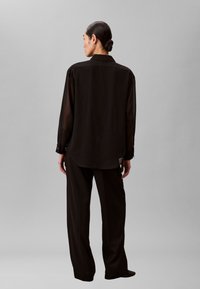 Sort transparent skjorte med knapper, krave, løs pasform og lange ærmer, kombineret med matchende vidde bukser. Simpelt design og blød tekstur.