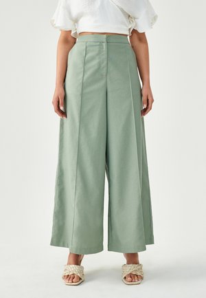 Lichtgroene wijde pijpenbroek van gladde stof met een hoge taille, voorzien van plooien aan de voorkant en een getailleerde pasvorm, gecombineerd met gevlochten sandalen.