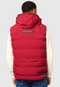 Chaleco de plumas rojo con capucha desmontable, diseño acolchado, parche con logo en la parte posterior y un bolsillo en la parte baja de la espalda. Fabricado en material sintético.