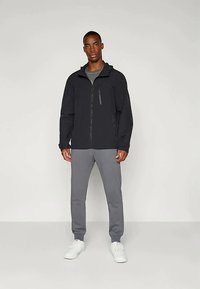 Juodas zip-up švarkas su pritaikytu dizainu, priekinis užtrauktukas ir šoniniai kišenės, derinamas su pilkais sportiniais kelnėmis ir baltais sportbačiais.