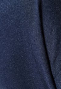 Detailní záběr na námořnickou modrou látku s měkkou, těsně tkanou texturou, která vykazuje mírné přirozené záhyby a jemné barevné variace.