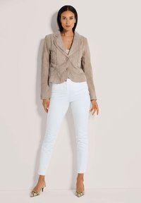 Taupe Wildleder-Blazer mit Reverskragen, zwei Knöpfen und geschwungenen Nähten, kombiniert mit hellblauen Skinny Jeans und gemusterten spitzen Schuhen.