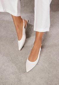 Valged slingback kortsandaalid terava nina kujundusega, sile nahk ja minimalistlik siluett. Pehme sisemine vooder ja madal konts.