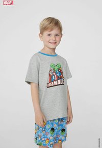 Graues Baumwoll-T-Shirt mit blauen Akzenten, das ein Marvel-Graphic von Superhelden und das Wort "ASSEMBLE" zeigt. Blaue Shorts mit bunten Superhelden-Motiven.