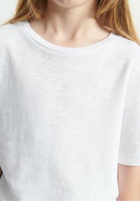 Balta trumpa rankovė t-shirt pagaminta iš lengvos medžiagos, turi apvalią iškirptę ir glotnų paviršių, tinkama kasdieniam dėvėjimui.