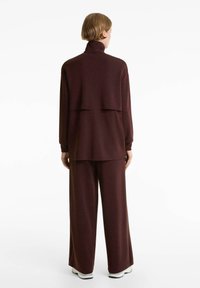 Bordeaux tweedelige set met een hoog gesloten pullover en een broek met wijde pijpen, gemaakt van zachte stof. De pullover heeft een gelaagd ontwerp aan de achterkant.