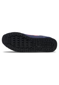 Black rubber sole of a sneaker with deep tread, accented with blue and red fabric upper. Features a logo imprint near the heel.