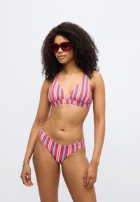 Svītrains bikini ar V veida izgriezuma bralete augšdaļu un apaļām biksītēm sarkanā, zilā un baltā krāsā. Gluda auduma un pieguloša dizaina.