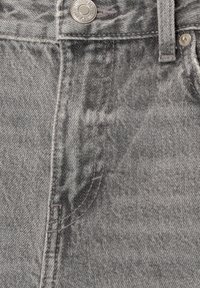 Harmaa denim-kangas, jossa on sileä tekstuuri, metallinen nappi vyötäröllä, näkyvät ompeleet ja prominentein etutasku.